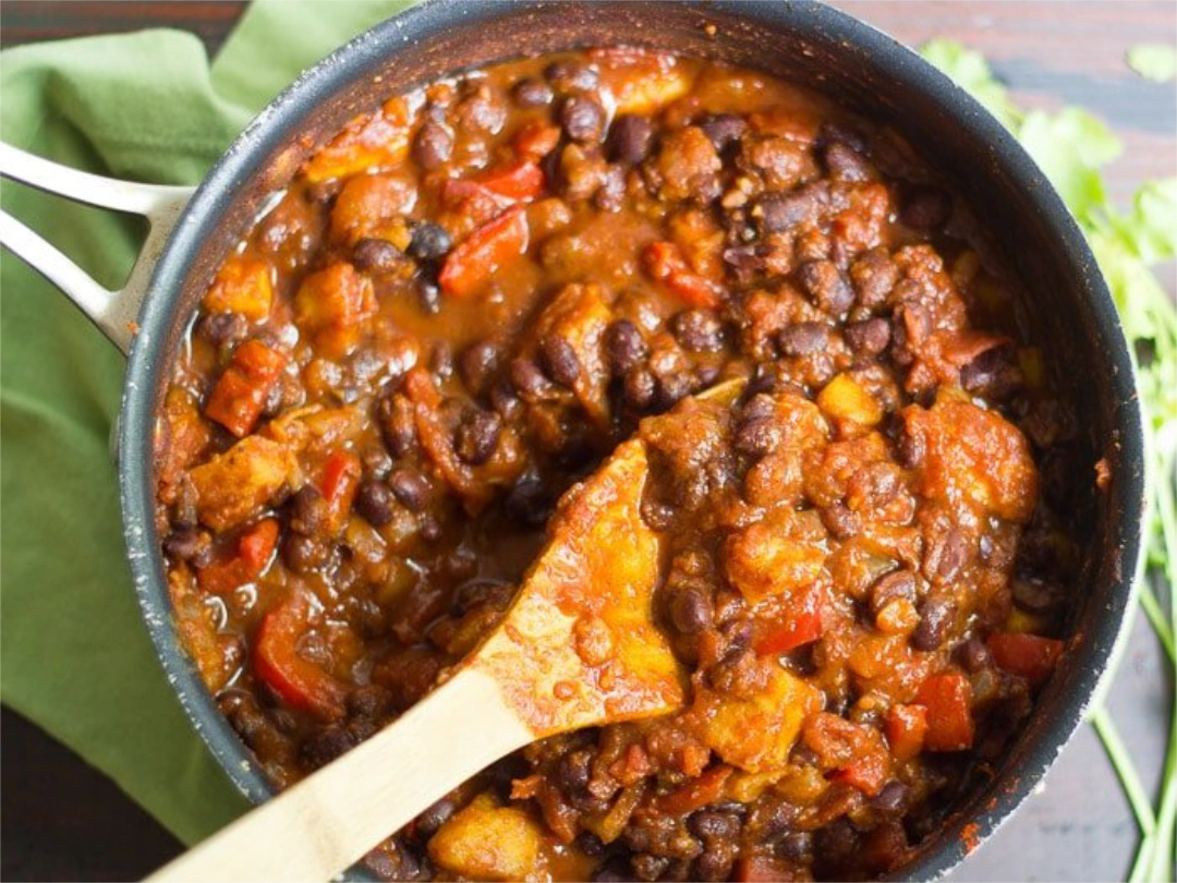 Black bean plantain chili stirred with a wooden spoon in a skillet
