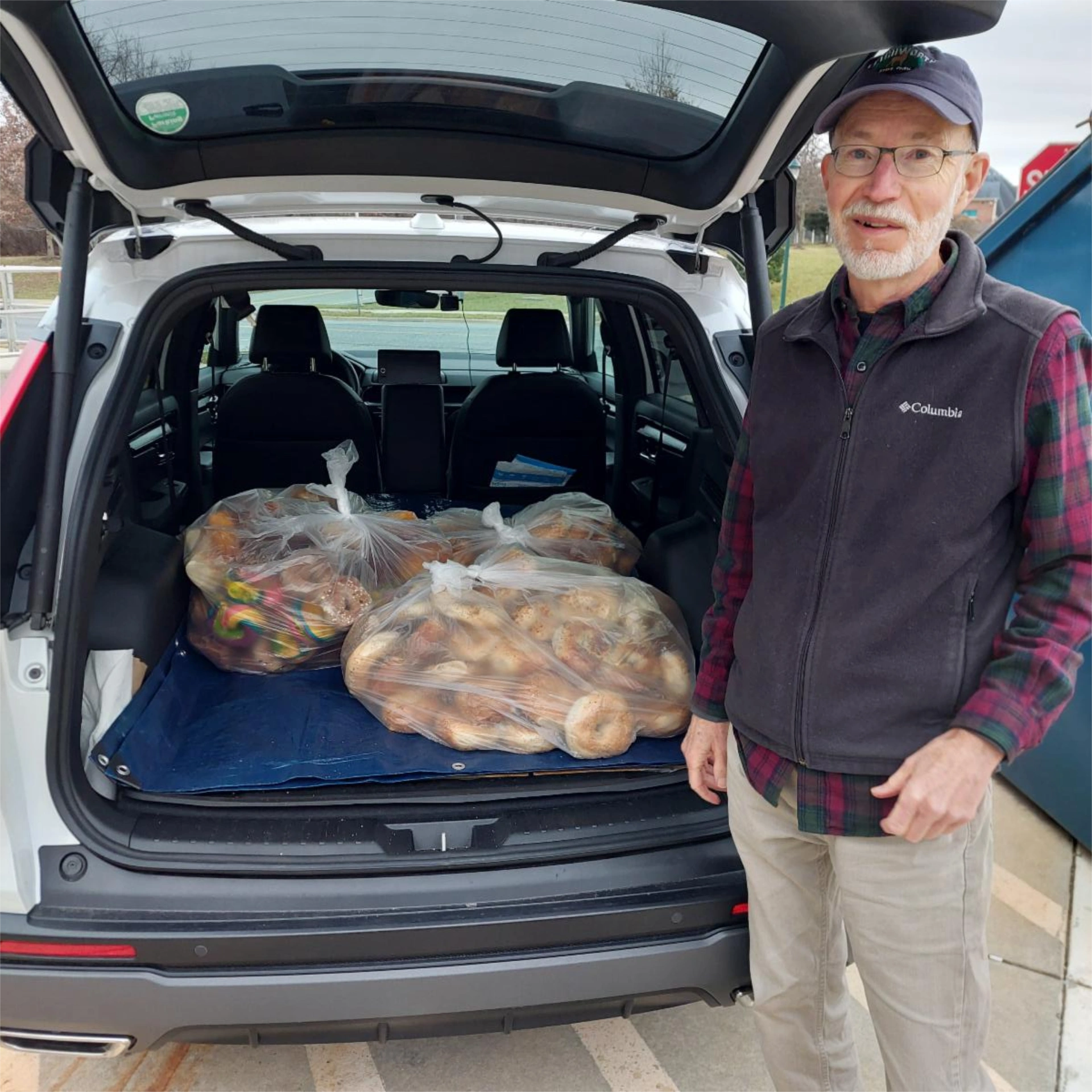 Manna volunteer in front of car trunk with bags of rescued pastries and breads