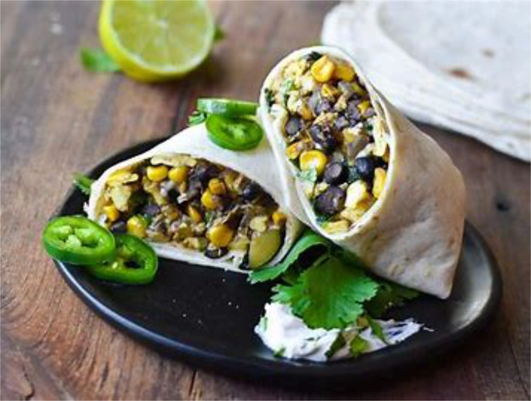 Burrito cut in half with one half slanted on top of the other, with cilantro leaves and slices of jalapeño as garnish