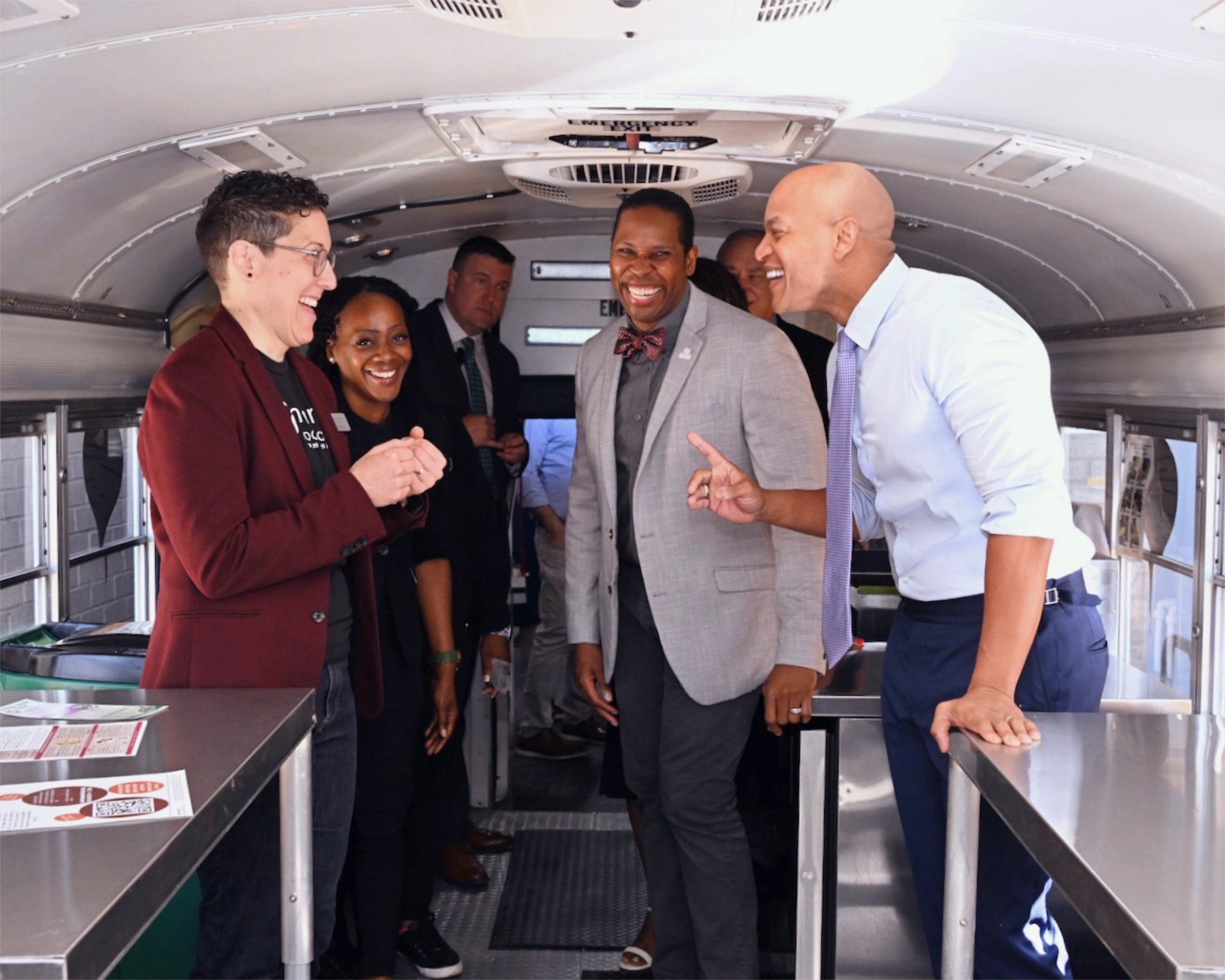 Craig, Jenna, and Mardia smiling at event on school bus with Governor Wes Moore