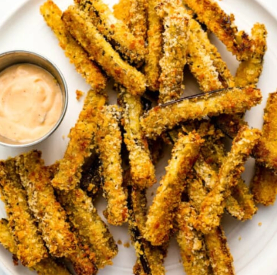 Pile of crispy eggplant next to a small dish with dressing