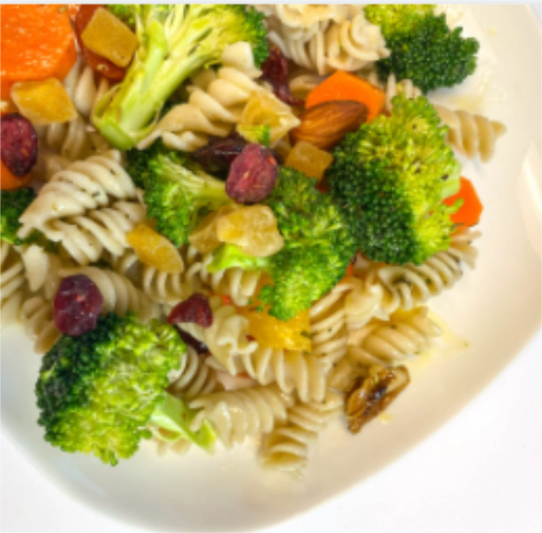 A mixture of rotini pasta with broccoli, peppers, and cranberries