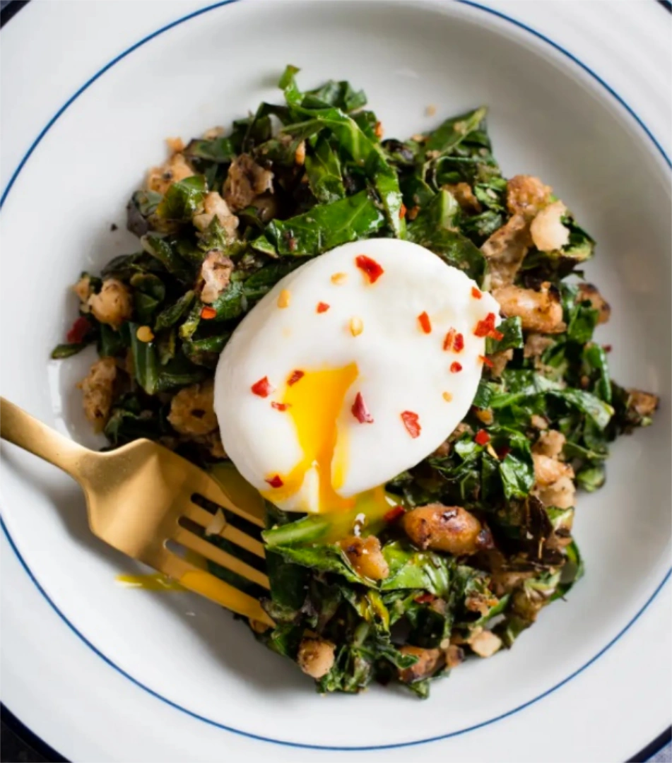 Poached egg on top of plate of greens and beans hash
