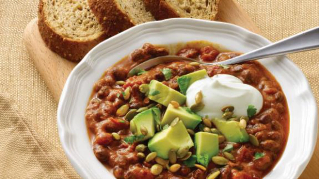 A bowl of chili topped with avocado chunks and a dollop of sour cream