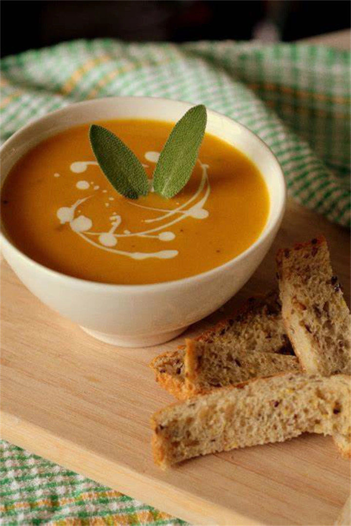 A bowl of pumpkin soup next to three pieces of bread