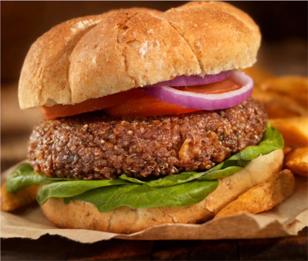 A quinoa patty with onion on top of spinach within burger buns