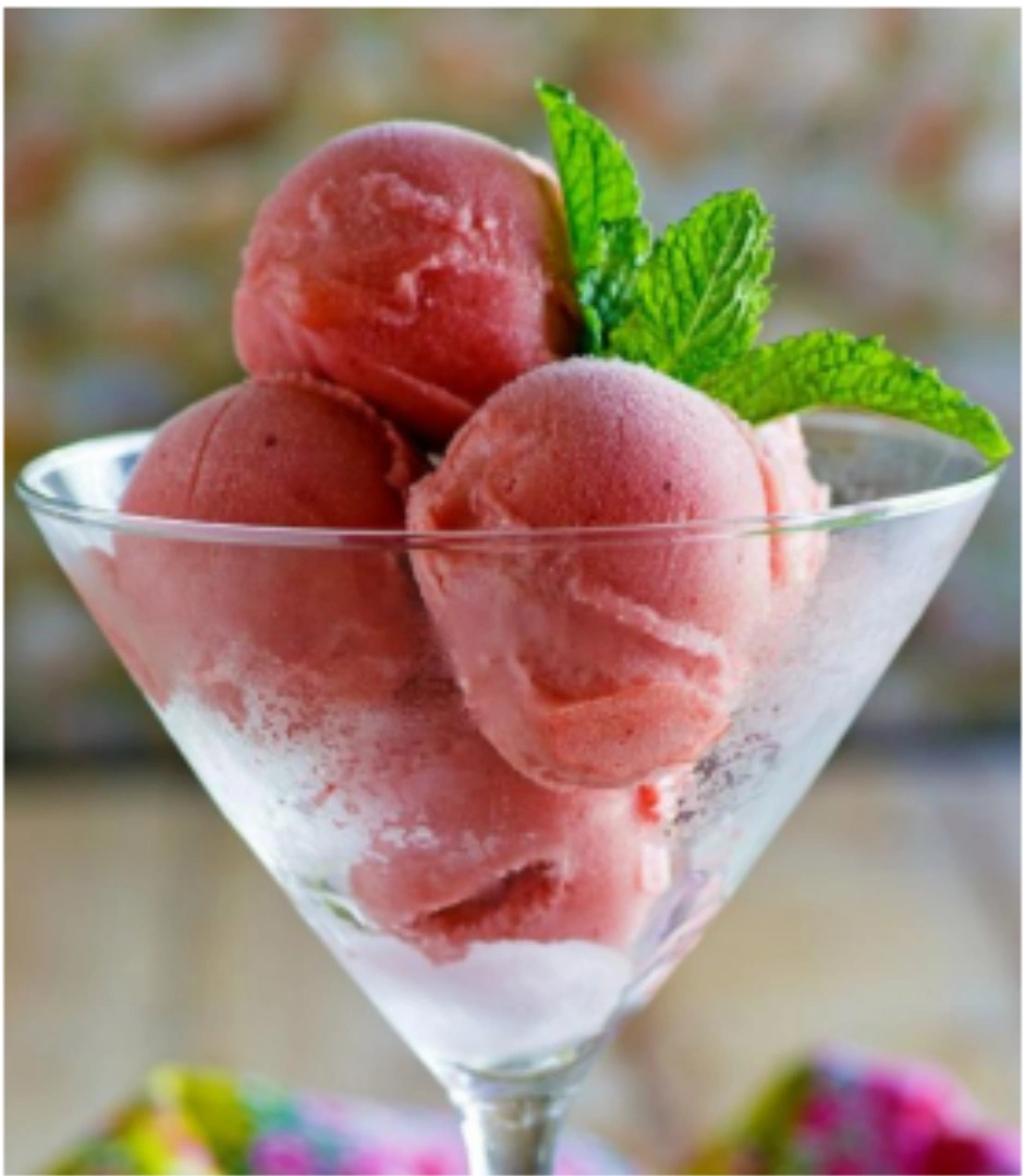 A martini glass with three scoops of watermelon sorbet and sprig of mint
